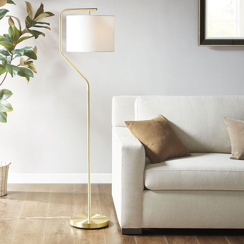 Gold angular arched metal floor lamp with white drum shade beside beige sofa in modern living room