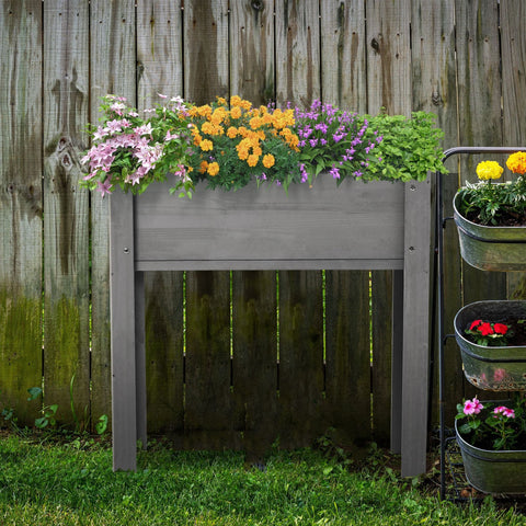 Grey raised garden bed with legs made of solid wood, filled with colorful flowers, standing on grass against a wooden fence