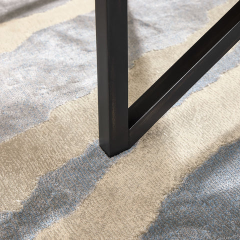 close-up of black wood base leg on modern simple glass coffee table on beige and blue patterned rug