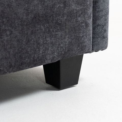 Close-up of dark grey chenille fabric sofa leg with black tapered wooden base on white floor, part of ultra-soft XXXL 3-seater sofa