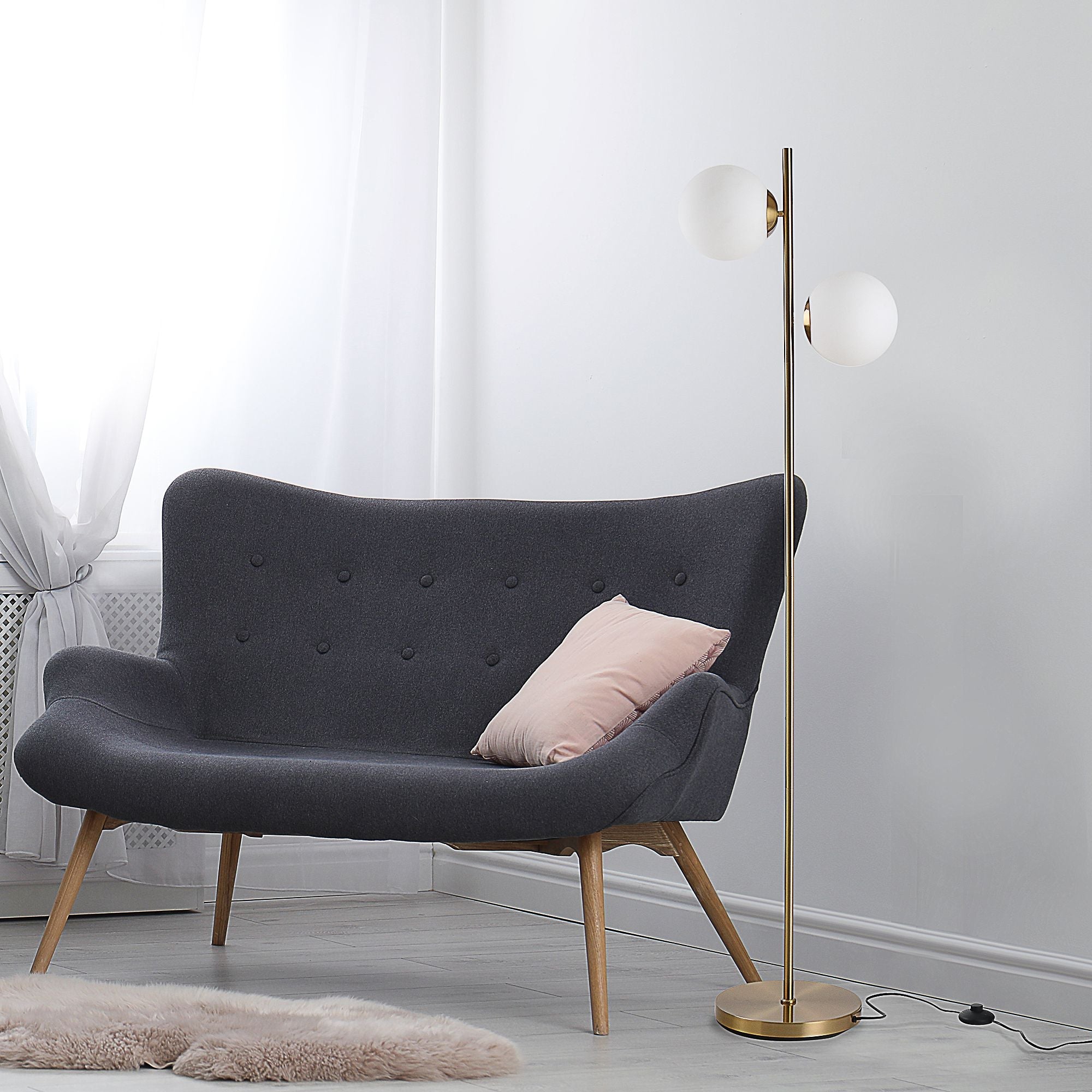 HOMCOM decorative floor lamp with two white glass globe shades, gold metal body, stable round base, and footswitch, placed beside a dark gray sofa in a modern living room.