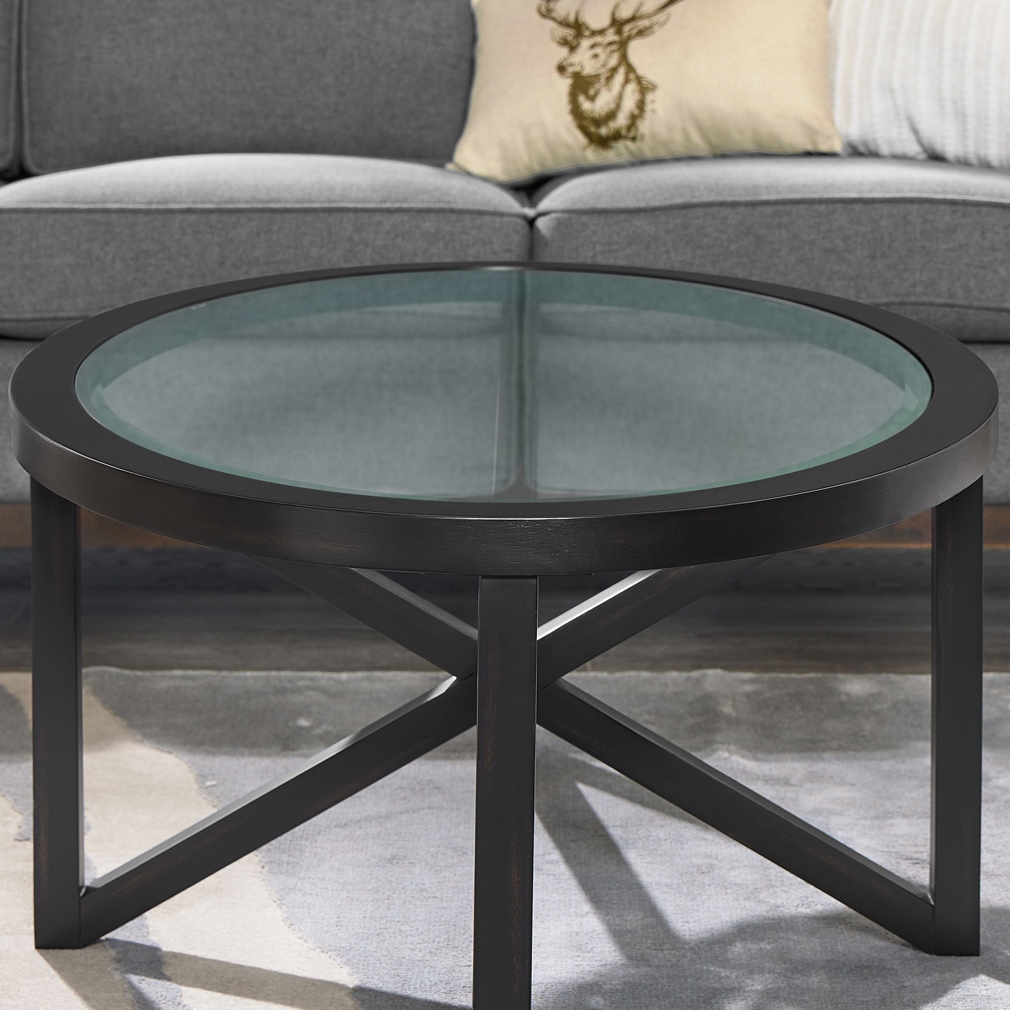 Round modern simple glass coffee table with black solid wood base and clear tempered glass top in living room setting